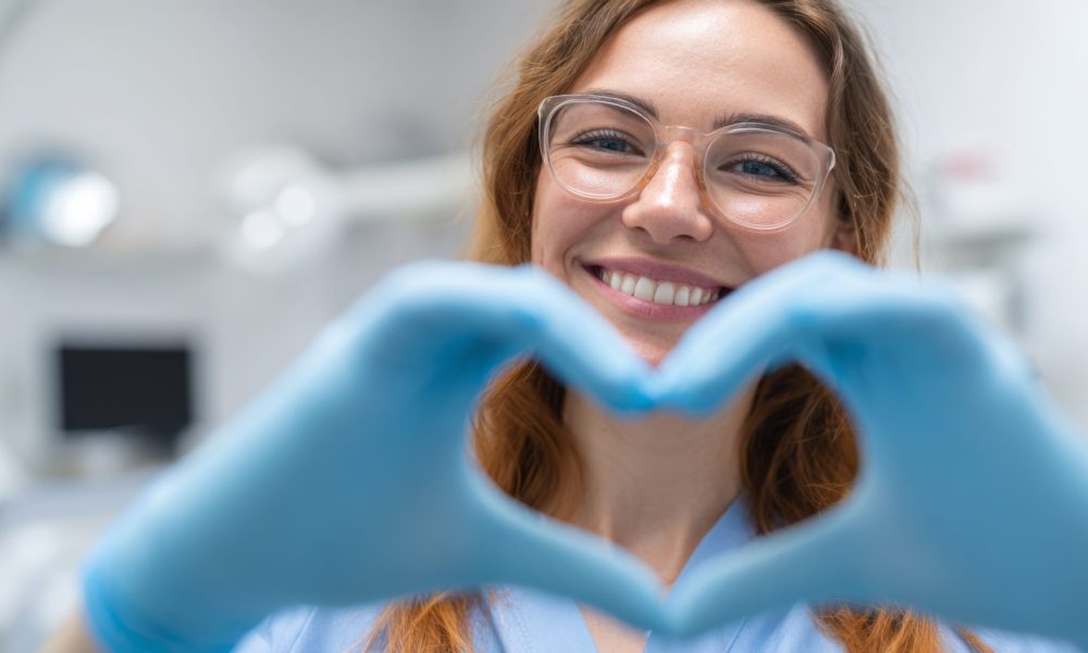Dentist woman smiling and making heart shape with gloved hands in clinic
