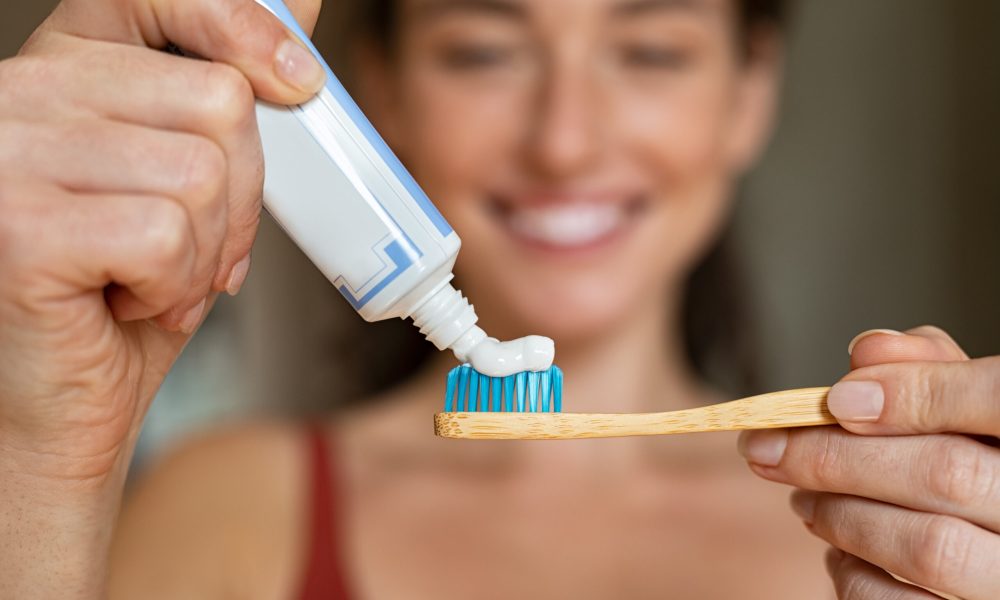 Close up of woman with tooth brush applying paste in bathroom. Closeup of girl hands squeezing toothpaste on ecological wooden brush. Smiling beautiful woman applying toothpaste on eco friendly toothbrush.