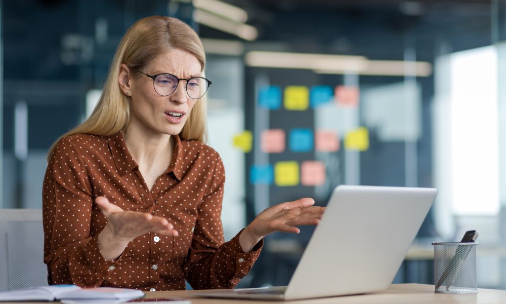 Anxious and nervous woman working with laptop inside office at workplace. Businesswoman got error and computer lock. Bad news with financial failures.