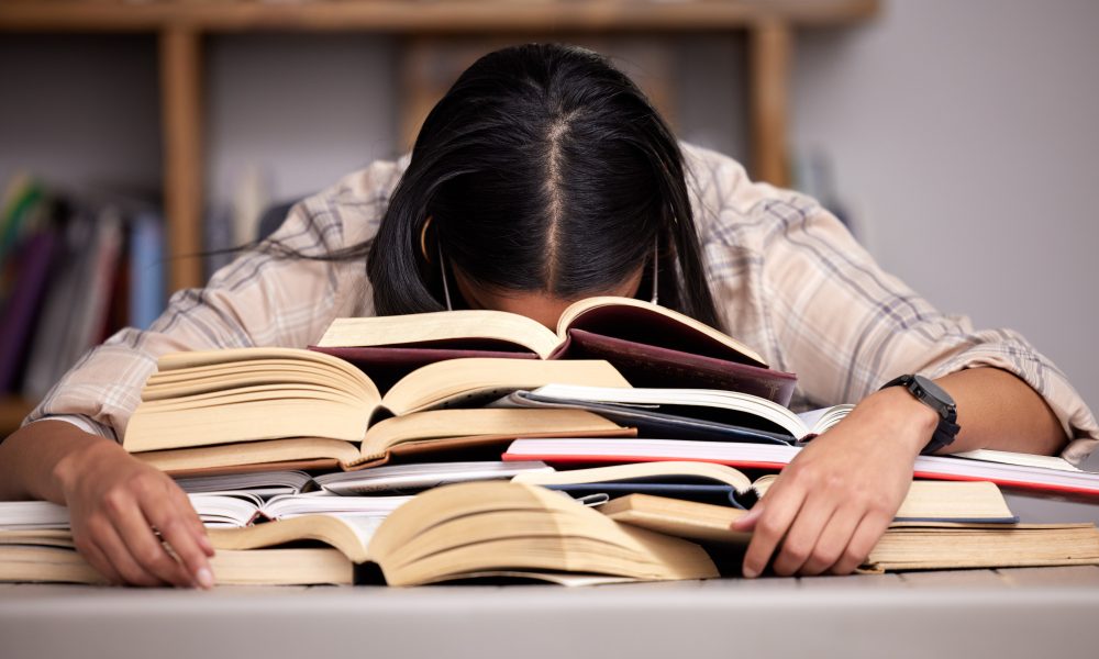 Study books, fatigue and woman student at desk with textbook for test feeling overworked. Stress, female person and home studying for university exam and course with burnout and sleeping in a house.
