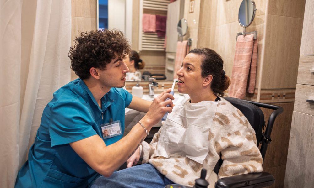 Professional caregiver helping a woman with a disability in a wheelchair to brush her teeth, promoting personal hygiene, independence, and well being in a bathroom setting